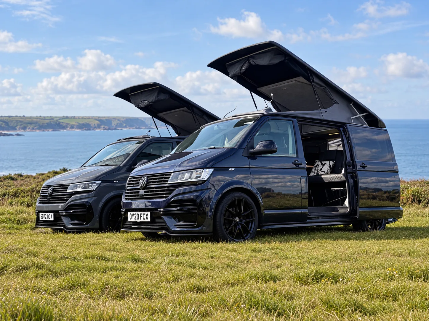 Two Vanlord campervans with raised pop-top roofs beside the coast